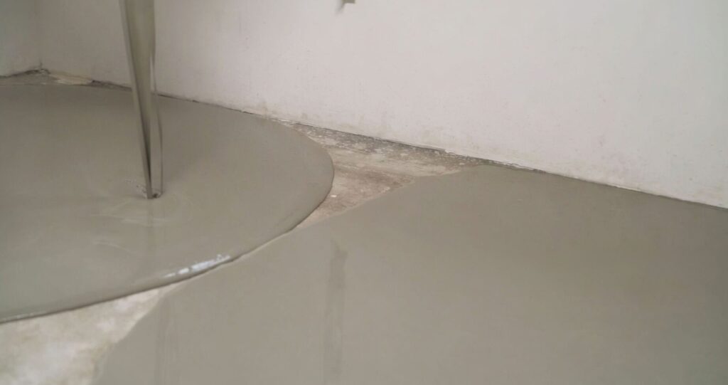 Worker applying self-leveling mortar on floor surface